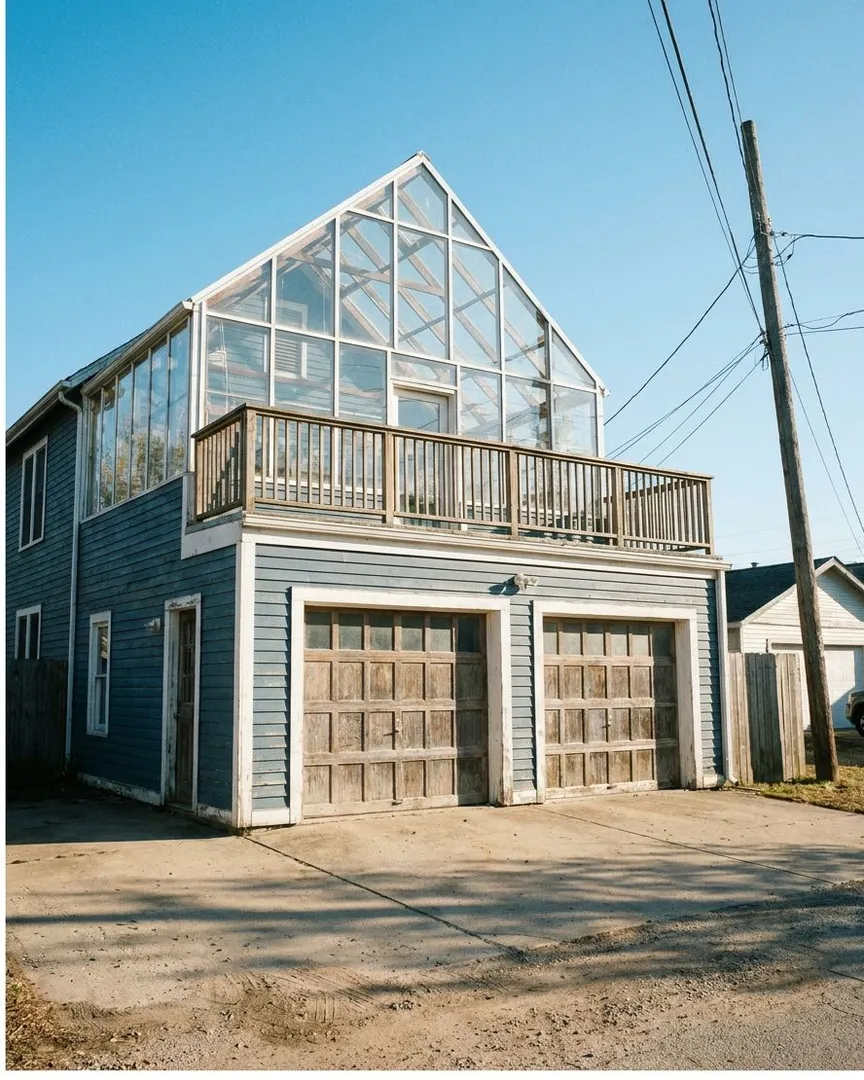 A two-story blue house with a large glass greenhouse built on top of the garage.