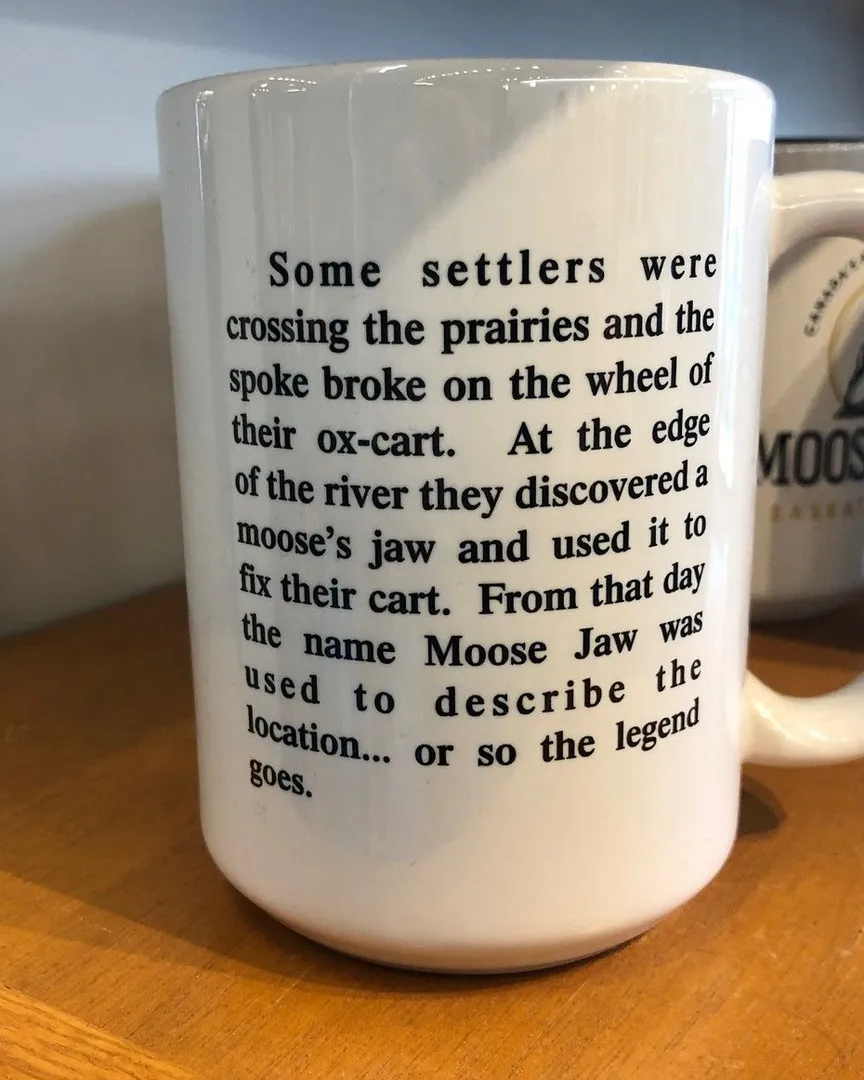A white ceramic mug with printed black text sitting on a wooden shelf.
