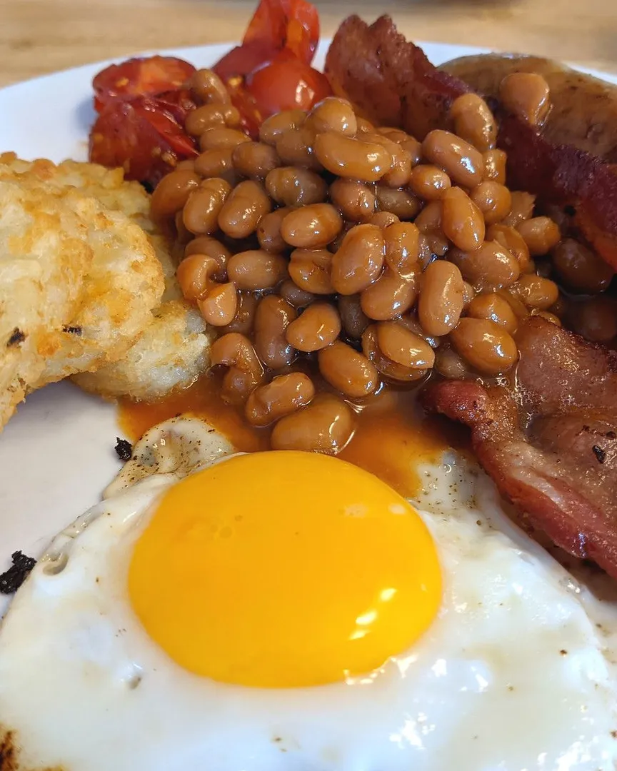 A close-up shot of a breakfast plate with a fried egg, baked beans, and bacon.