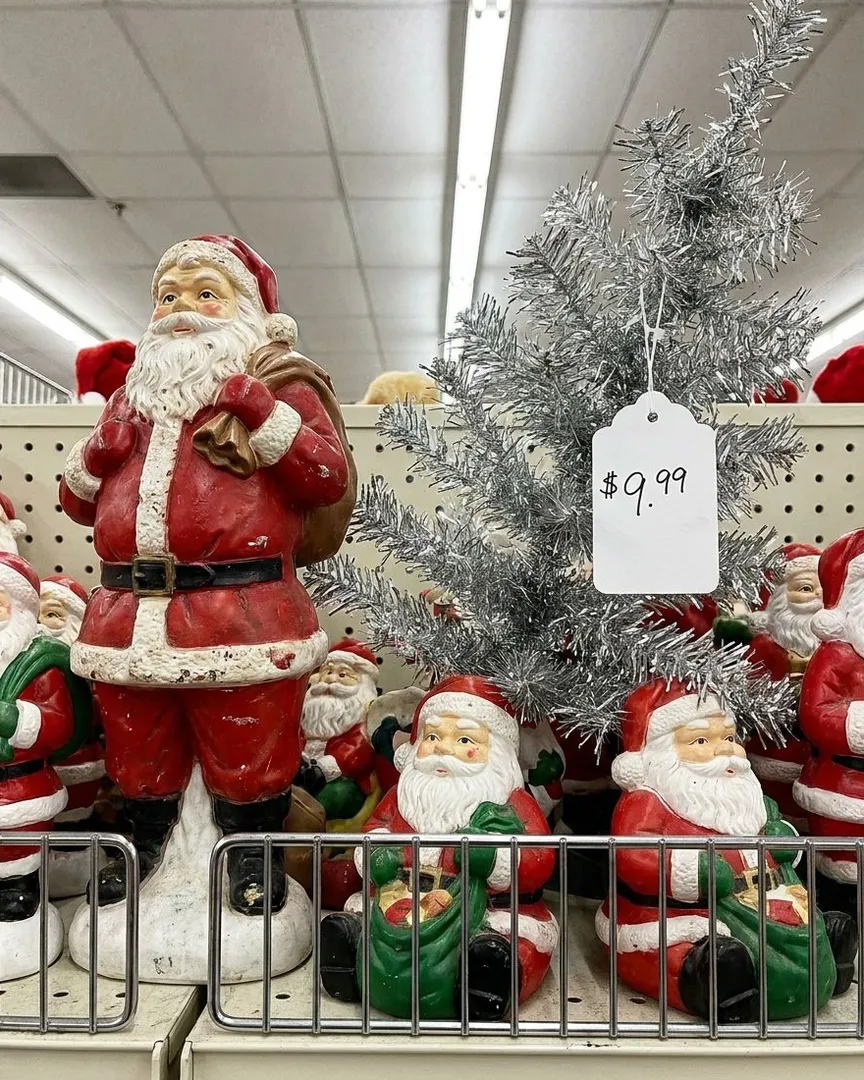 A shelf in a store filled with vintage Santa Claus figurines and a small silver tinsel tree.