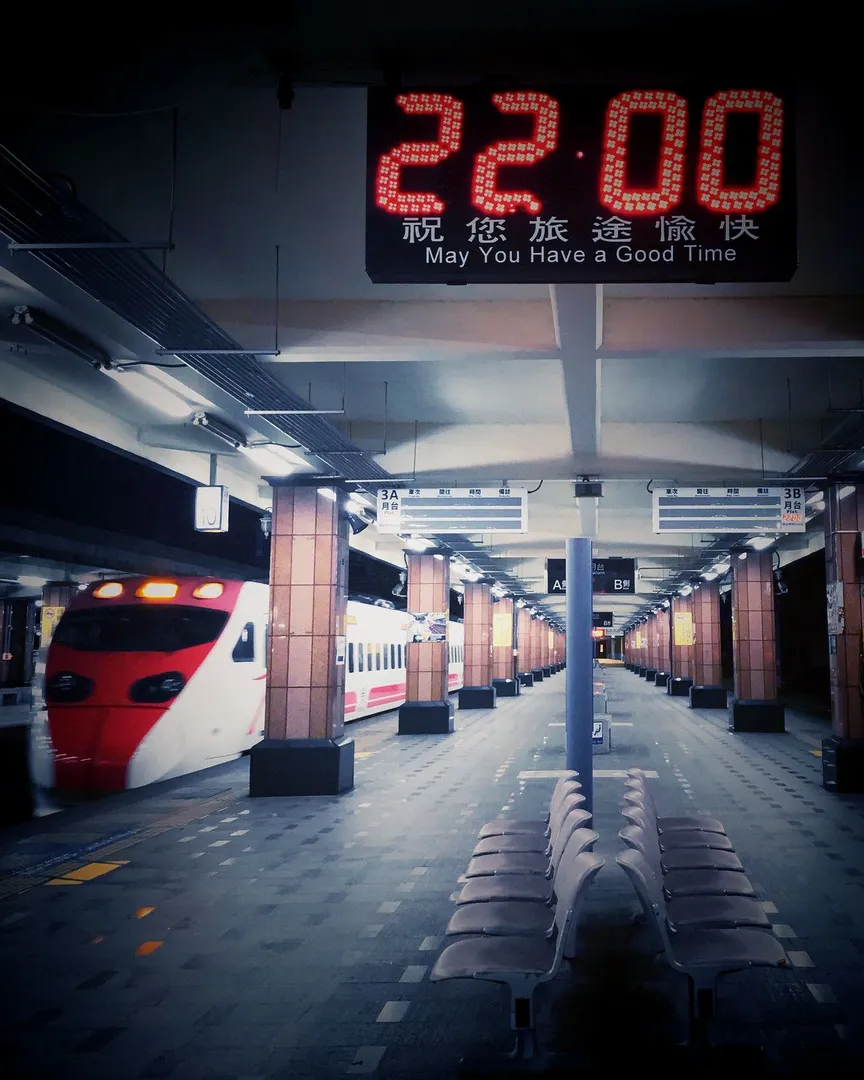 An empty train platform at night with a red and white train and a digital clock.