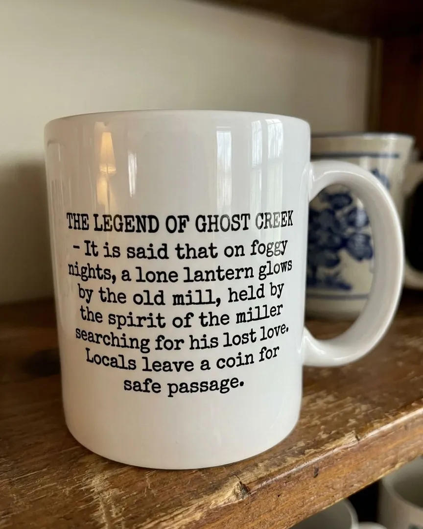 A white ceramic mug with printed black text sitting on a rustic wooden shelf.