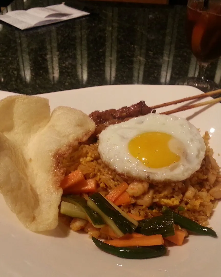 A plate of Indonesian fried rice with a fried egg, satay skewers, and crackers.